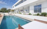 Villa in Vista Talamanca 6 Ibiza – Large Villa Rental Ibiza Main Description Large villa rental Ibiza, Villa in Vista Talamanca 6 Ibiza is a modern contemporary property located in the desirable village of Jesús, just minutes from Ibiza Town and Talamanca Beach. Designed with clean architectural lines and elegant finishes, this stylish villa offers privacy, comfort, and a prime location close to the beach. Prime Location Near Talamanca Beach & Ibiza Town Moreover, the villa is centrally positioned in Jesús, one of the most sought-after residential areas in Ibiza. As a result, guests can easily reach supermarkets, restaurants, and local services within minutes. At the same time, Talamanca Beach, Marina Botafoch, and Ibiza Town are only a short drive away, offering vibrant nightlife, exclusive restaurants, and luxury boutiques. Outdoor Living & Private Pool Area In addition, the villa features several covered and sun-drenched terraces distributed across different levels. The private swimming pool is located one level below the main living area and is surrounded by comfortable lounge beds. Furthermore, there is a covered outdoor dining terrace with a BBQ and outdoor bar, creating the perfect environment for relaxed afternoons and evening gatherings. The rooftop terrace offers additional space to enjoy open countryside views and the green landscape of Ibiza. Consequently, guests can choose between sun, shade, and panoramic views throughout the day. Contemporary Interiors & Functional Layout Inside, the villa combines velvet textures, wood finishes, and refined design elements. The open kitchen with a central cooking island flows seamlessly into the living and dining areas, creating a bright and welcoming space. Thanks to large windows and sliding doors, the interior connects naturally with the terraces and outdoor areas. The villa accommodates 8 guests across 4 bedrooms and 4 bathrooms, all designed with comfort and privacy in mind. Two bedrooms are located on the upper level, including the master suite with en-suite bathroom. The other two bedrooms are positioned on the lower level, each with independent entrances and en-suite bathrooms, providing additional privacy for guests. Overall, Villa in Vista Talamanca 6 Ibiza represents a refined large villa rental in Ibiza, ideal for families or small groups seeking modern comfort close to the beach and Ibiza Town. Accommodation & Rooms Sleeps up to 8 guests 4 bedrooms 4 bathrooms Master bedroom with en-suite bathroom and large closets Second bedroom with private bathroom Two lower-level bedrooms with independent entrances and en-suite bathrooms Air conditioning throughout Amenities & Features Private swimming pool Multiple terraces Rooftop terrace Covered outdoor dining area Outdoor bar & BBQ Fully equipped modern kitchen Sound system Satellite TV High-speed Wi-Fi Alarm system Laundry room Countryside views Private parking Location & Surroundings – Jesús & Talamanca, Ibiza Located in Jesús village Minutes from Talamanca Beach Close to Marina Botafoch Short drive to Ibiza Town Nearby supermarkets, restaurants, and gym Residential and family-friendly area Additional Services Available on Request To enhance your stay in Ibiza, we offer: Concierge services Private chef Extra cleaning Table service Massage and wellness treatments Nanny services Luxury car rental Yacht rental Private transfers All services can be arranged before arrival or during your stay. Villa Rental Rates (Per Week) Season Dates Price / Week Peak Season July & August € — High Season June € — Mid Season May & September € — Low Season April & October € — Minimum stay: 7 nights (Saturday – Saturday) Rental type: Weekly rental Technical Data & Specifications Property type: Modern contemporary villa Location: Jesús / Talamanca, Ibiza Guests: 8 Bedrooms: 4 Bathrooms: 4 Swimming pool: Private Air conditioning: Yes Internet: High-speed Wi-Fi Security: Alarm system Parking: Private Booking & Rental Information Welcome pack at arrival Cleaning: 2 hours per weekday + final cleaning Damage deposit: € 3,000 Booking policy: 50% down payment within 5 working days 50% one month before arrival Check-in: from 16:00 Check-out: before 10:00 No parties allowed